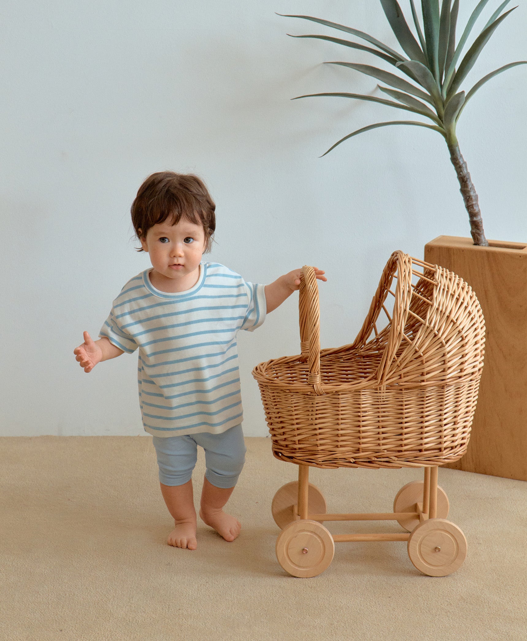 Baby boy in cute toddler boy clothes holding wooden cart